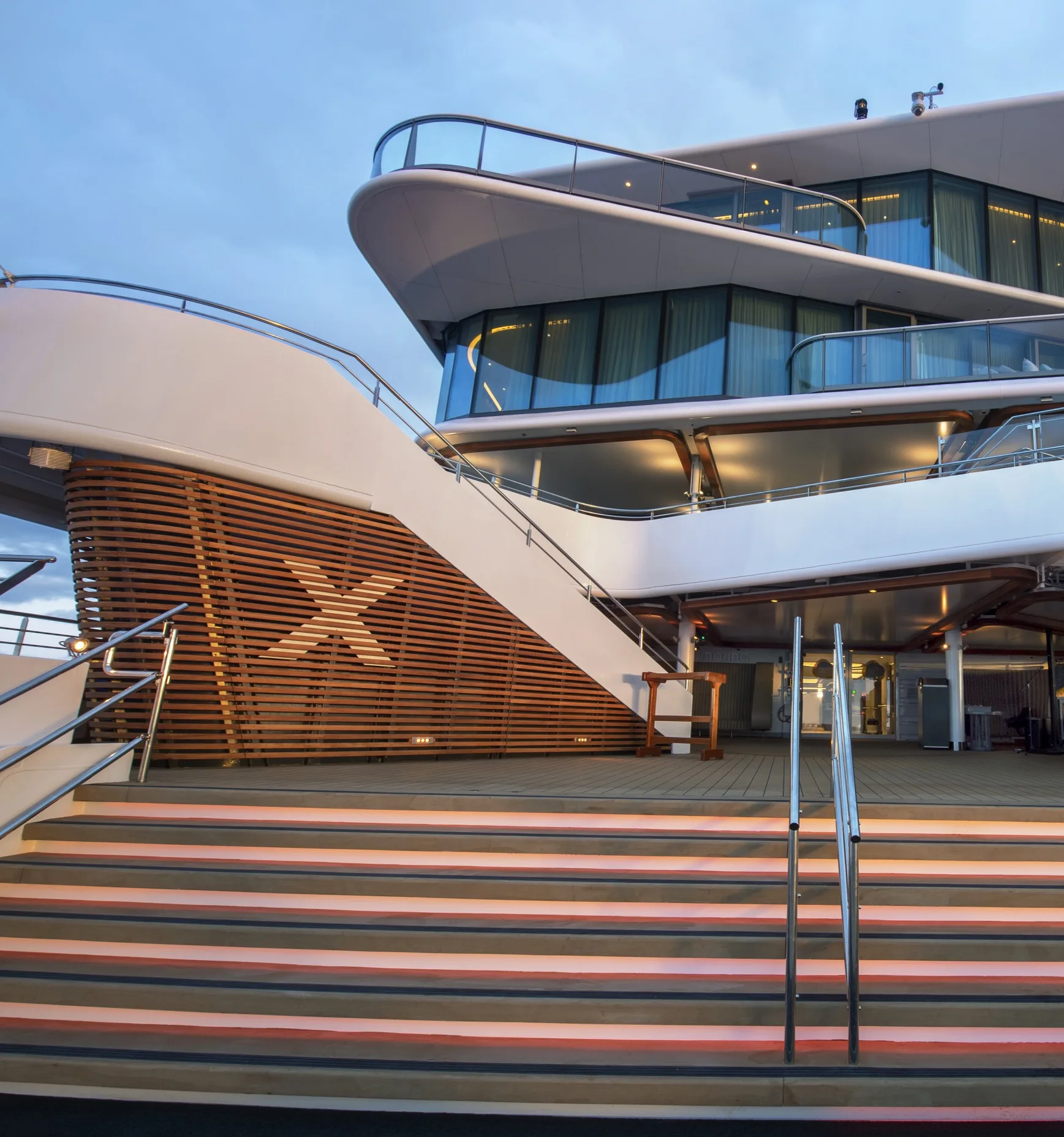Modern luxury cruise ship exterior with curved balconies, illuminated stairs, and sleek contemporary architecture.