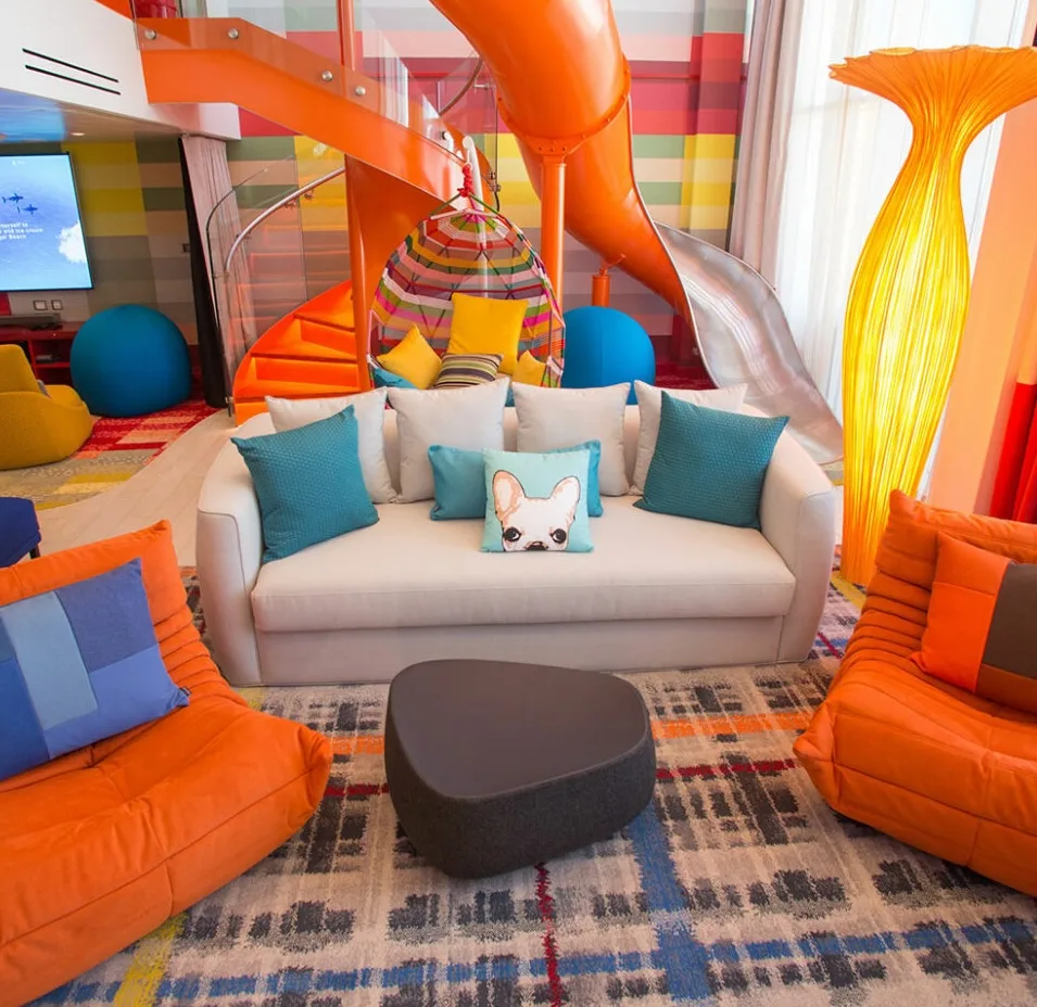 Colorful family hotel suite with indoor slide, modern lounge seating, and playful contemporary design.