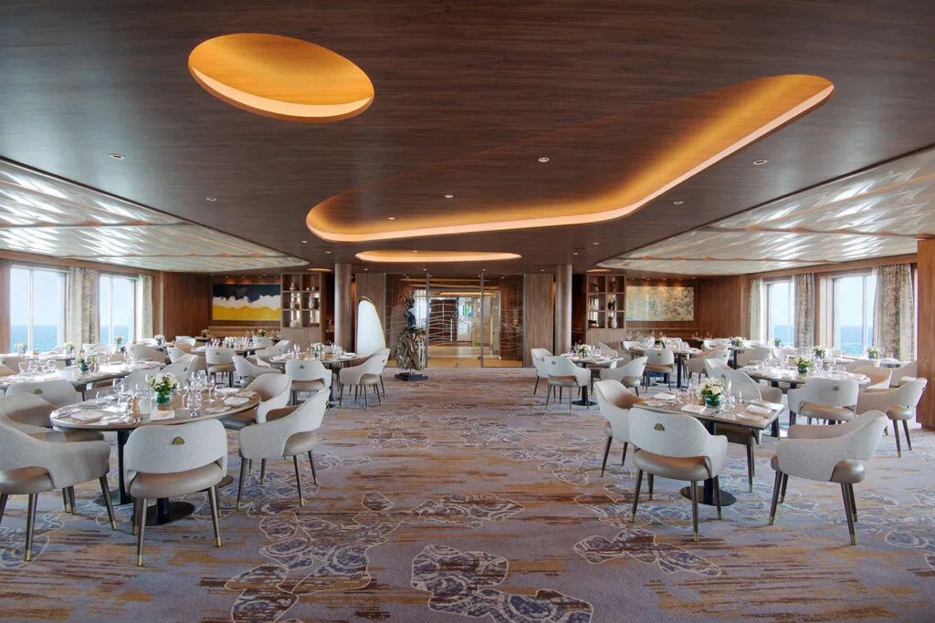 Bright ship dining room with curved ceiling lighting.